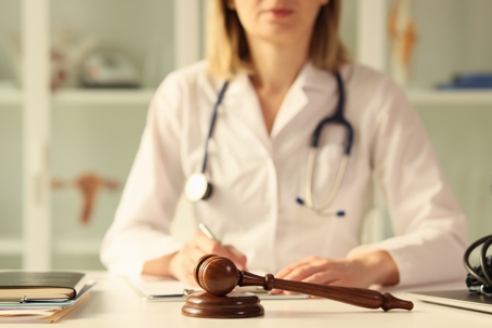 Close-up of wooden judge gavel on table female doctor doing paperwork on background. Litigation, malpractice and forensic concept