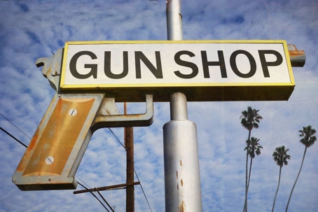 vintage sign for a gun shop against a blue sky and palm trees